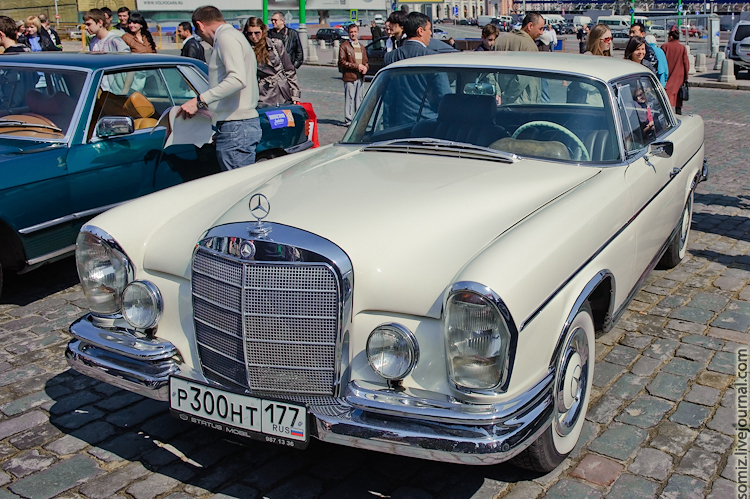 people are walking by an old mercedes car