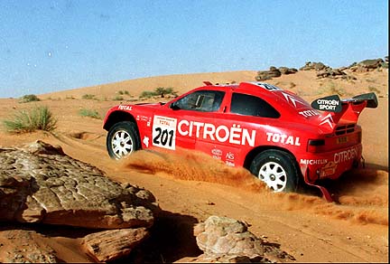 a red car that is driving in the sand