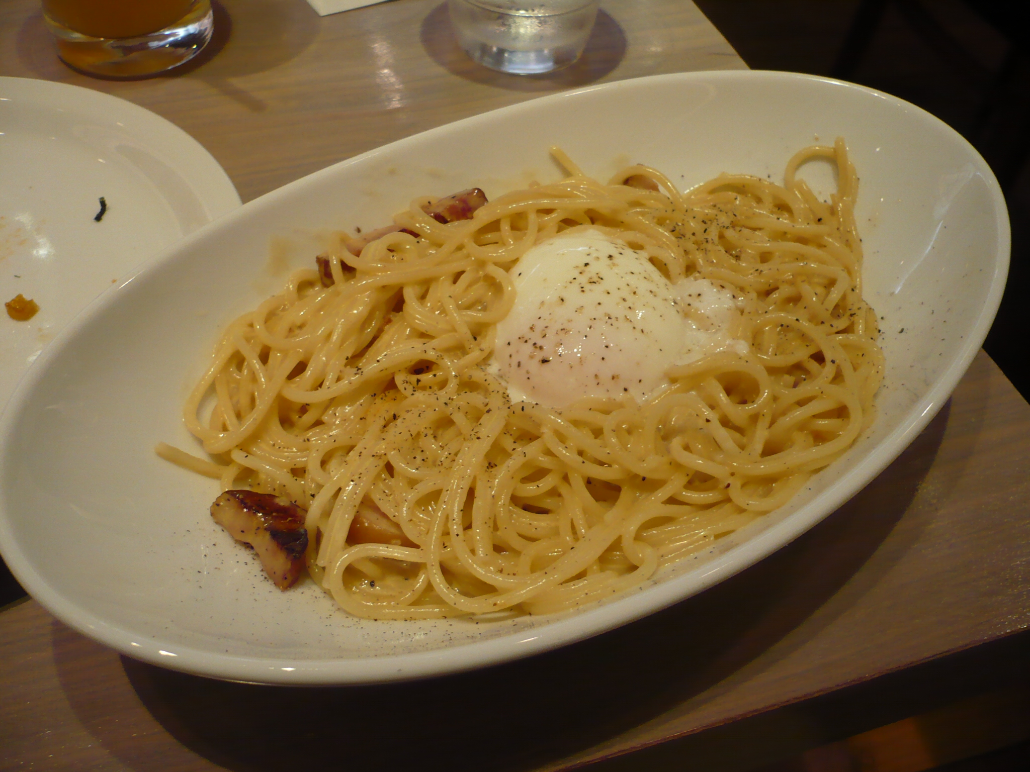 pasta with bacon and egg on top in white dish