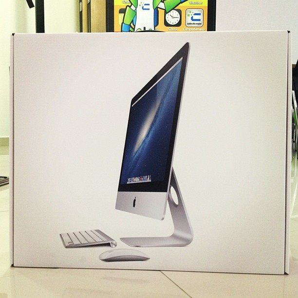 an apple desktop computer sitting in front of a poster for it's display