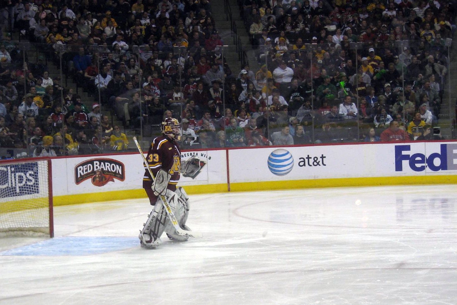 a hockey goalie with a glove on his head and people sitting behind him watching