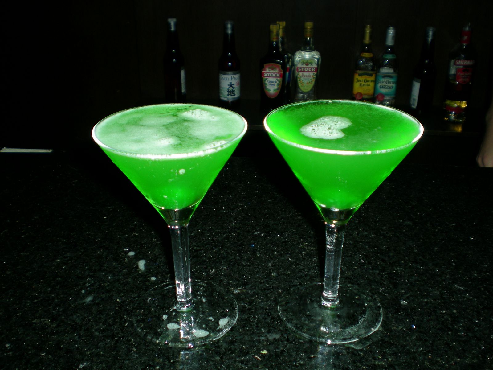 two martini glasses with green liquid are sitting on a counter