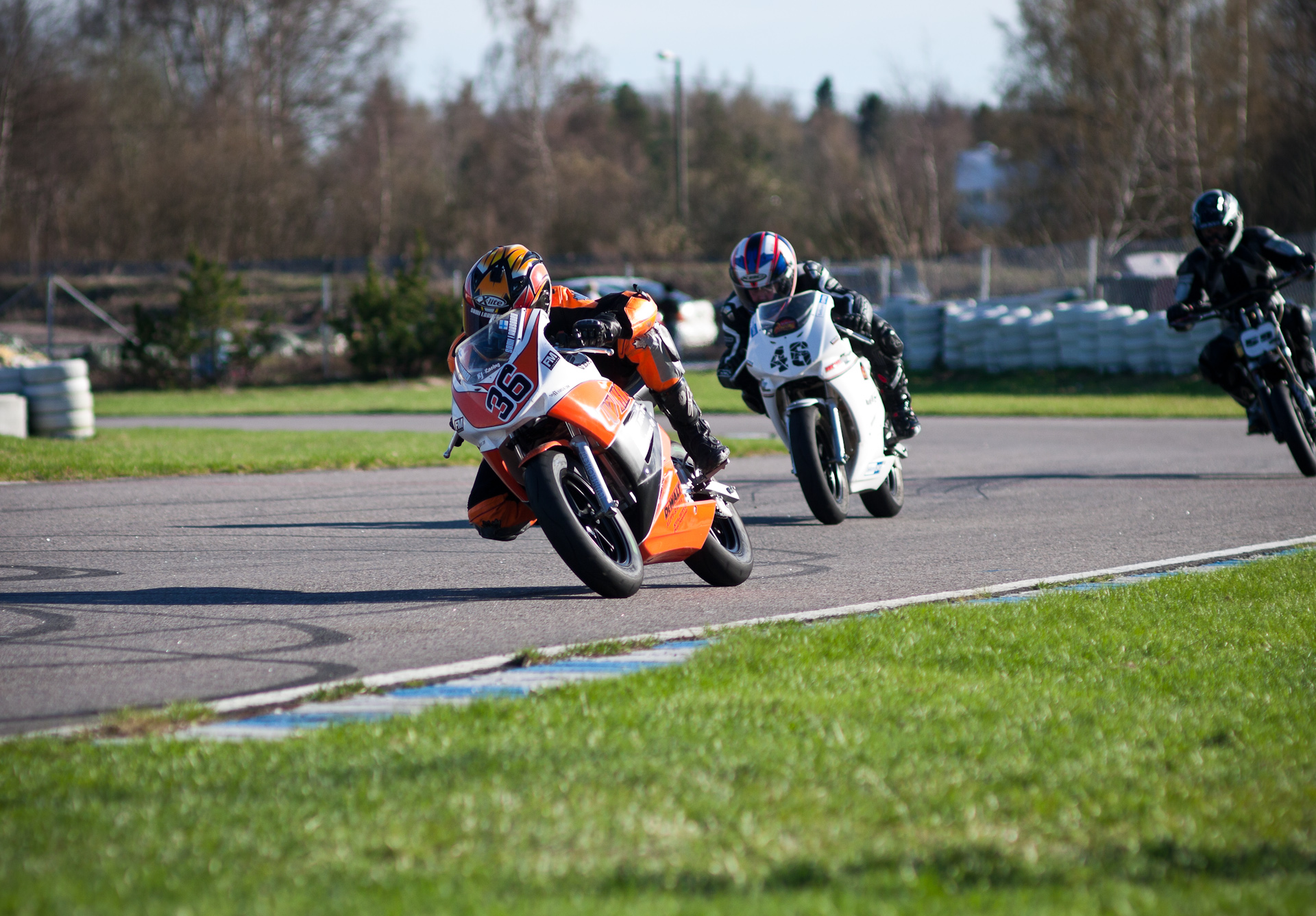 three motorcycles riding down a race track in a group