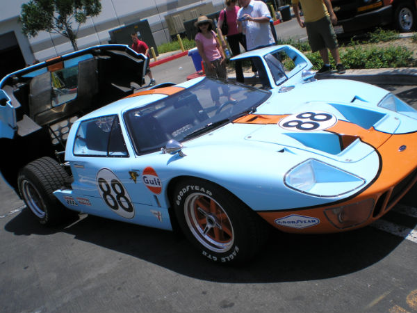 people stand in line at a parking meter next to a race car