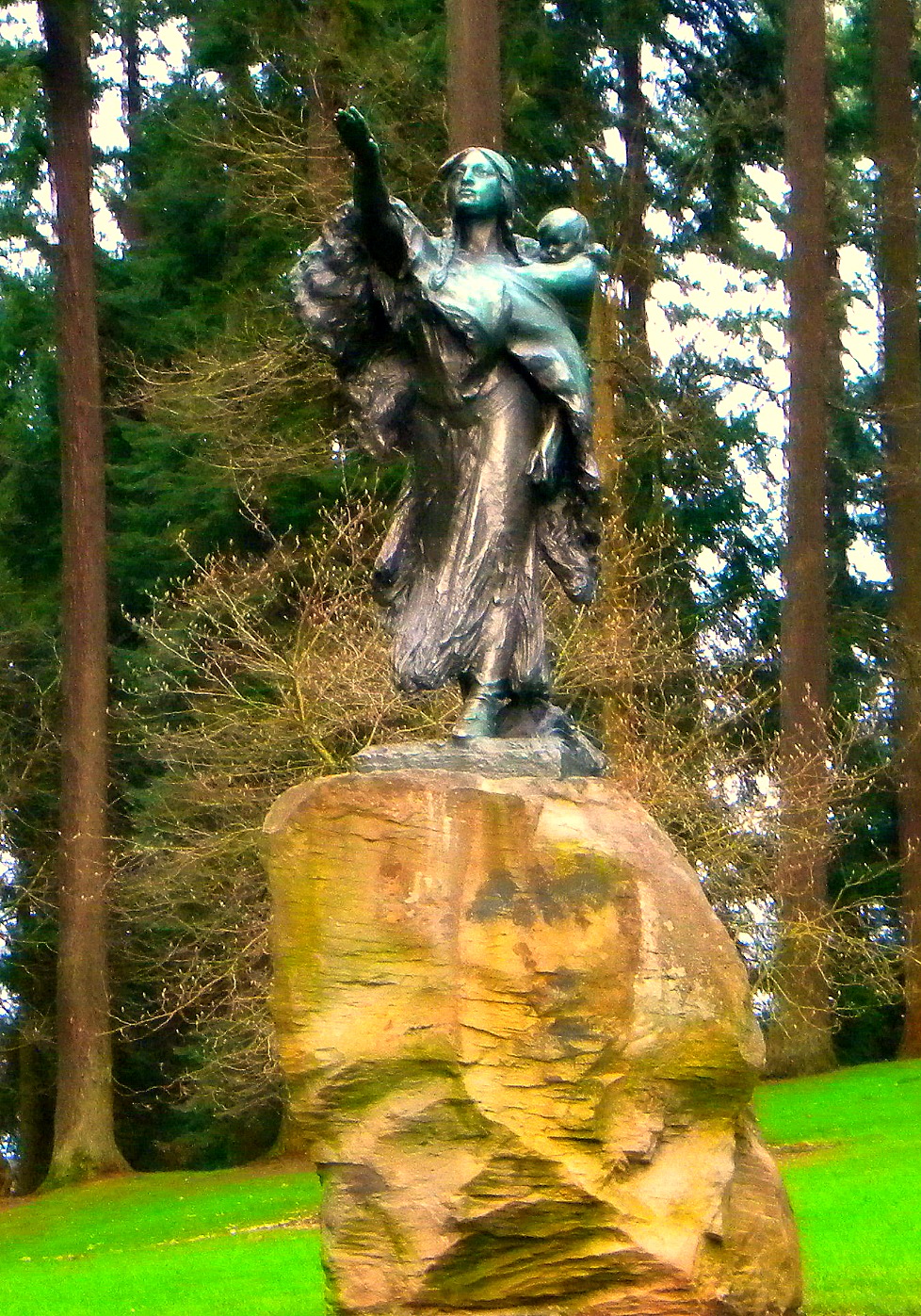 a statue sitting on top of a rock in the middle of a green field