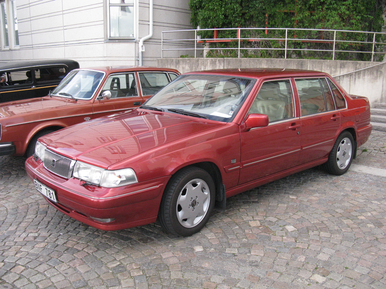 a couple of red cars are parked by a curb