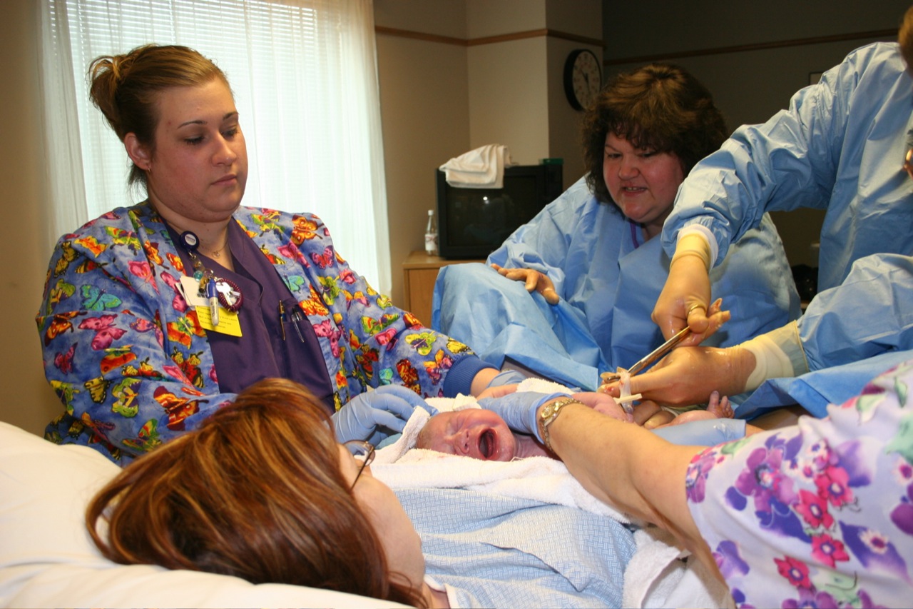 five woman in scrubs look at a baby