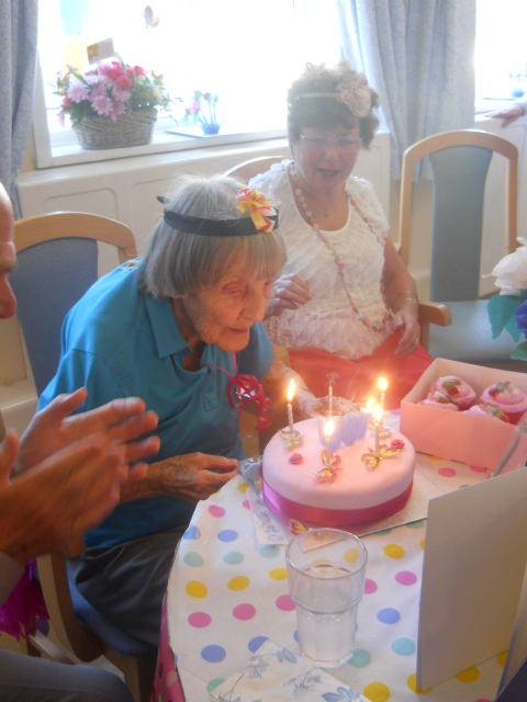 old woman blowing out candles on her birthday cake