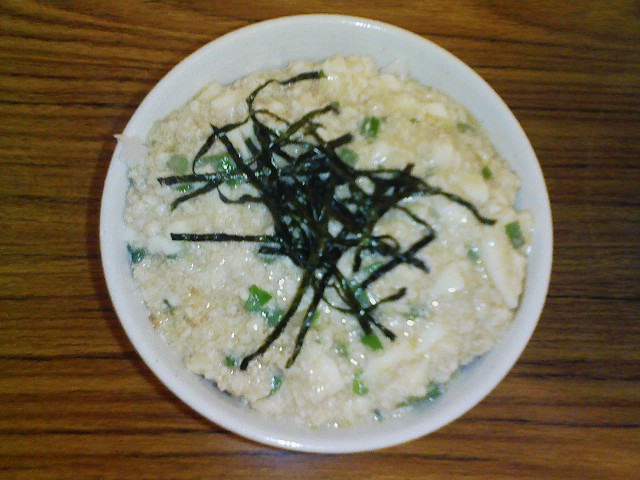 a white bowl containing rice, green onions and black sauce