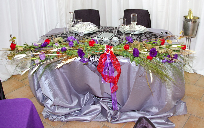 a table with a silver cloth over it that has purple and red flowers