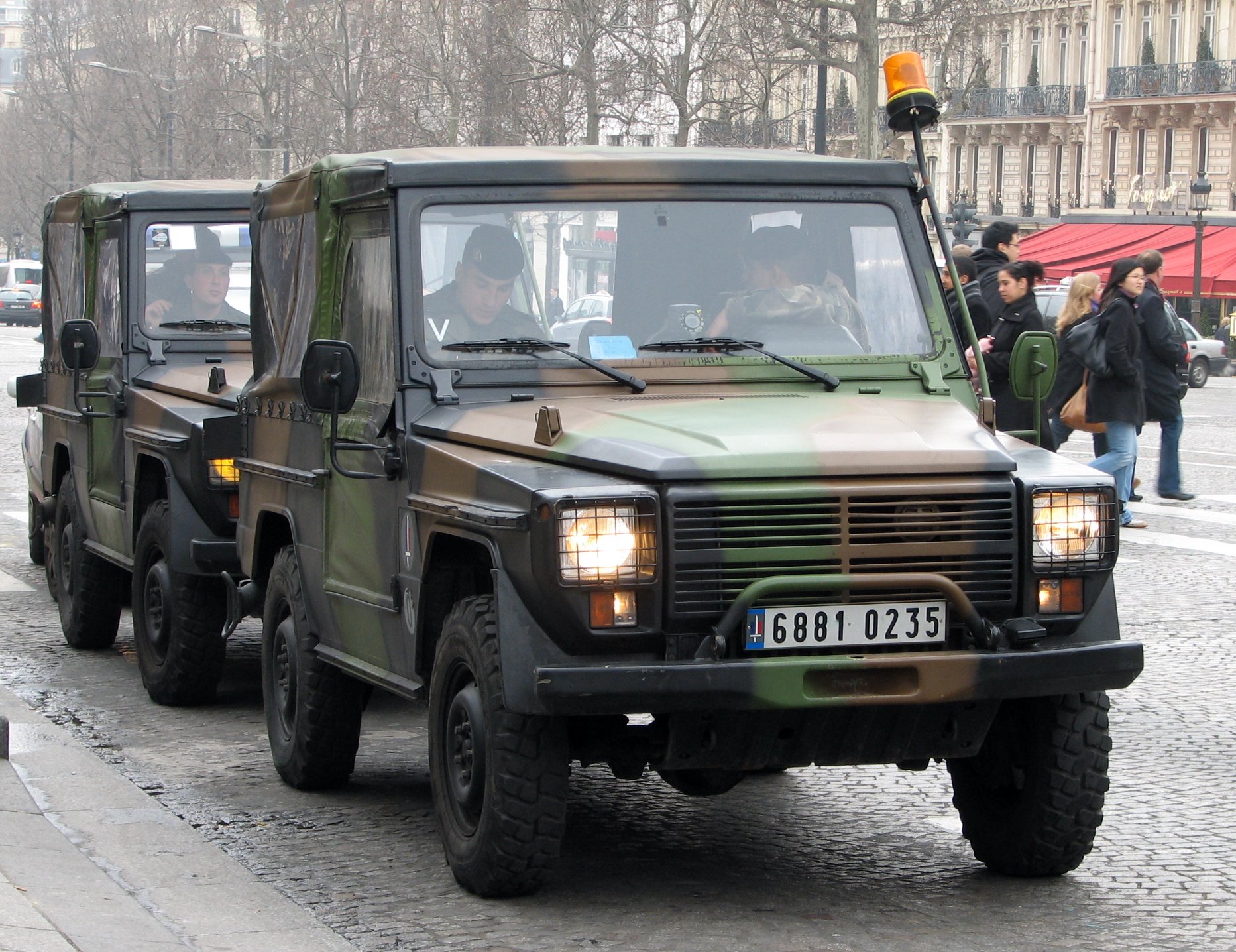 two military vehicles driving down the street with passengers in the back