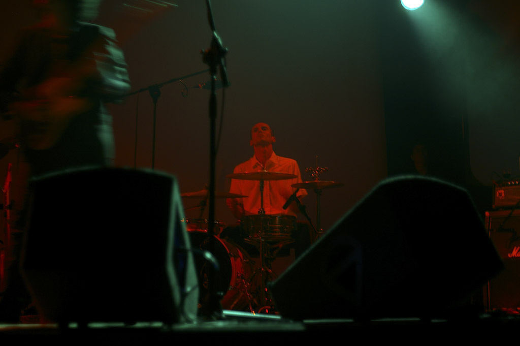 a musician stands before microphones on stage as another band plays in the background