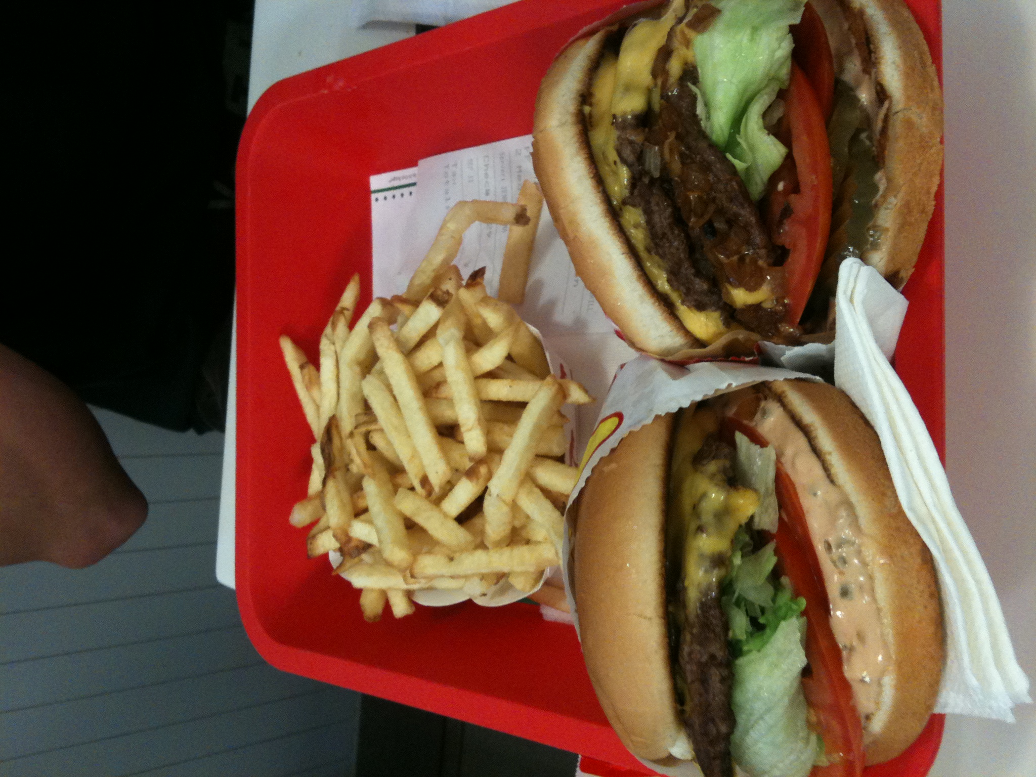 a red tray holds two hamburgers with fries on it