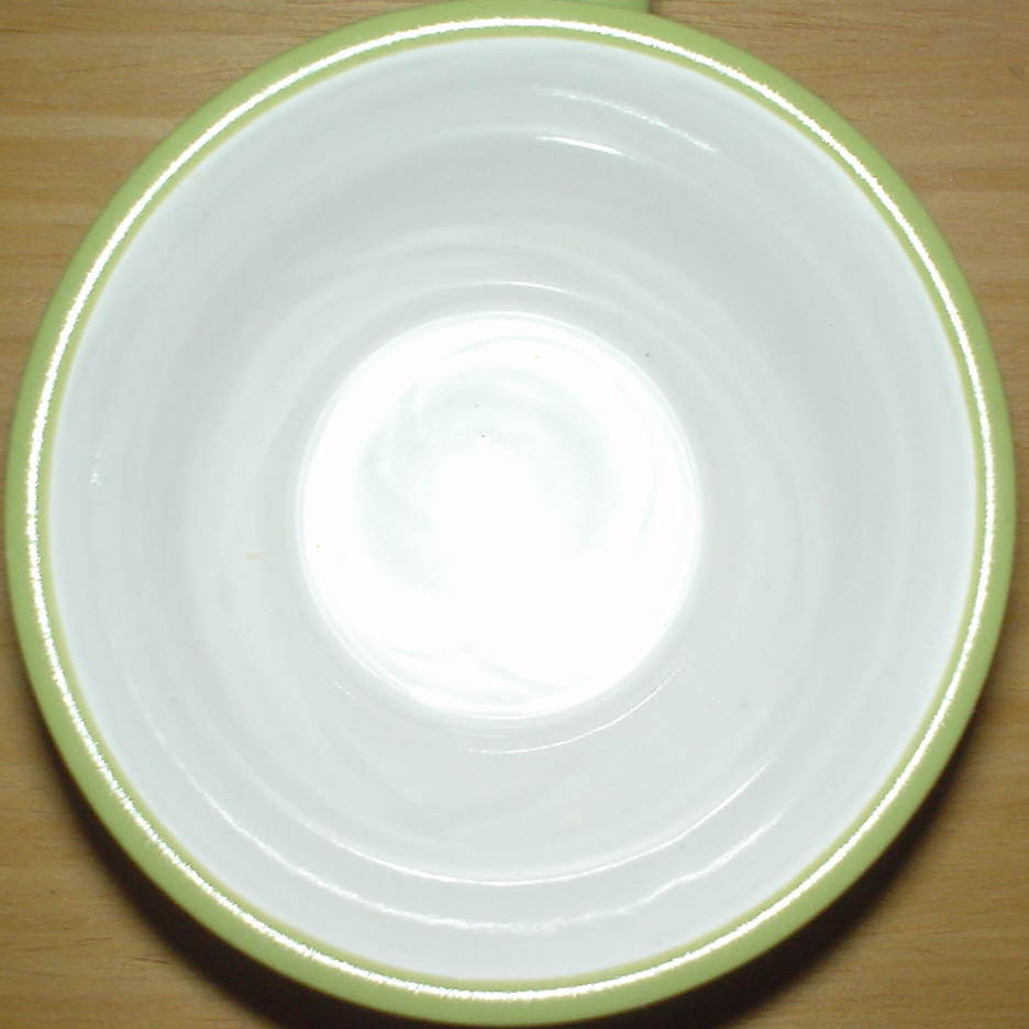 a white bowl with light green rim on a wooden surface