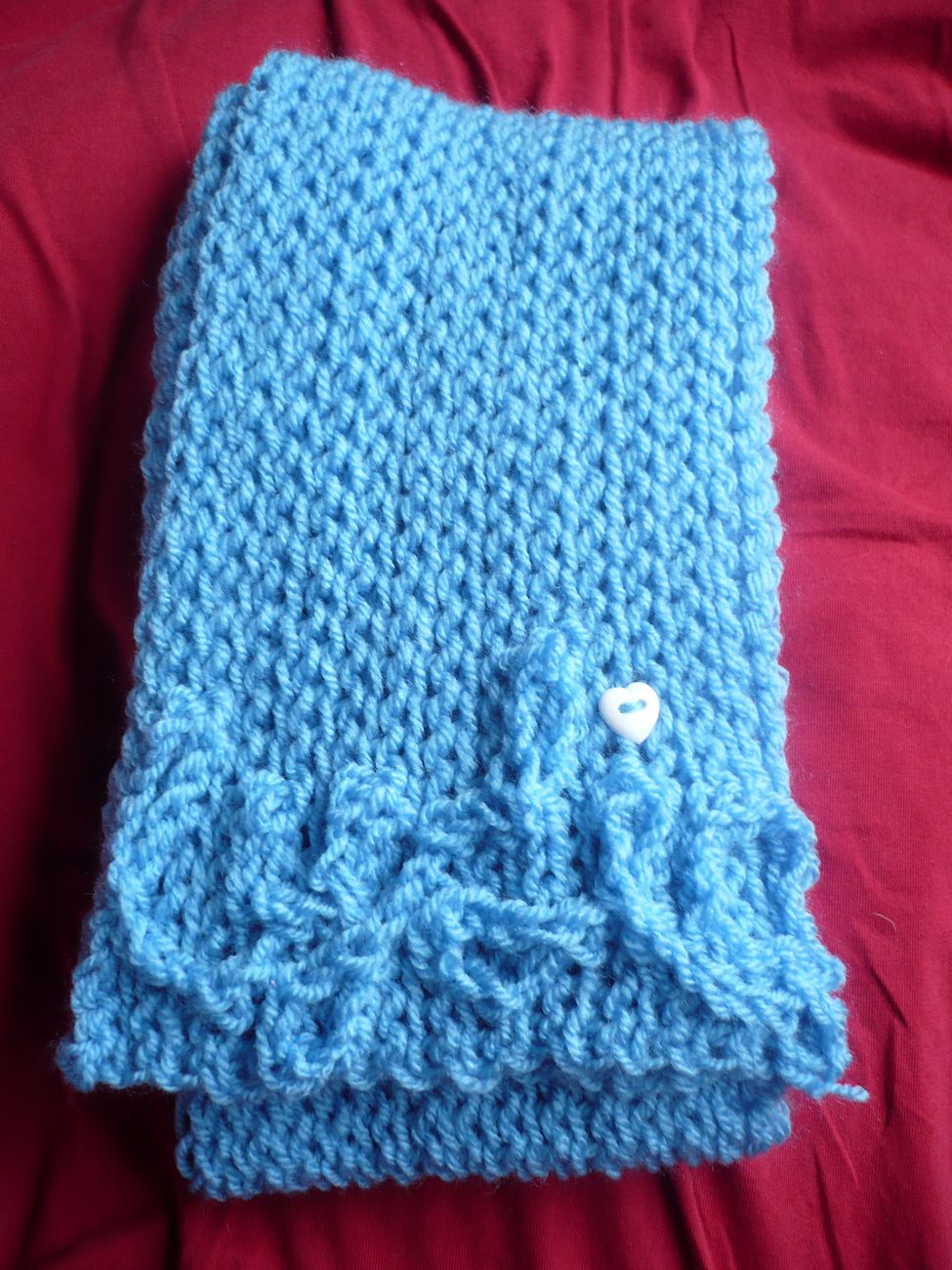 a knitted baby blue blanket on a red bed