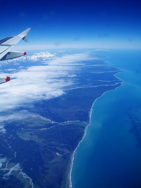 an airplane wing flying over the ocean and land