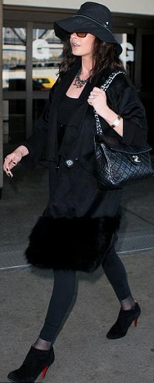 a woman in black is carrying a black purse and a black hat