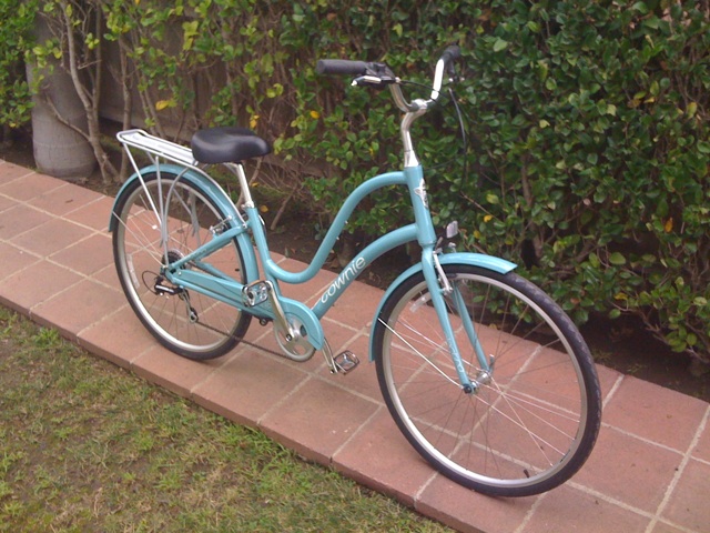 a blue bicycle on side walk with shrubbery behind it