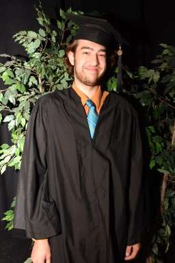 a man wearing a cap and gown with greenery around him