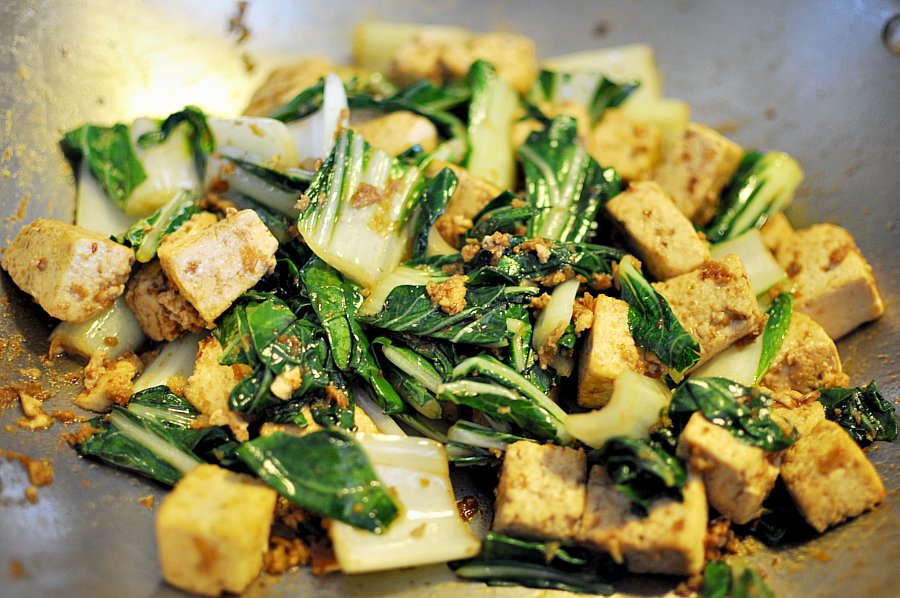 a stir fry in a wok with tofu, spinach and onions