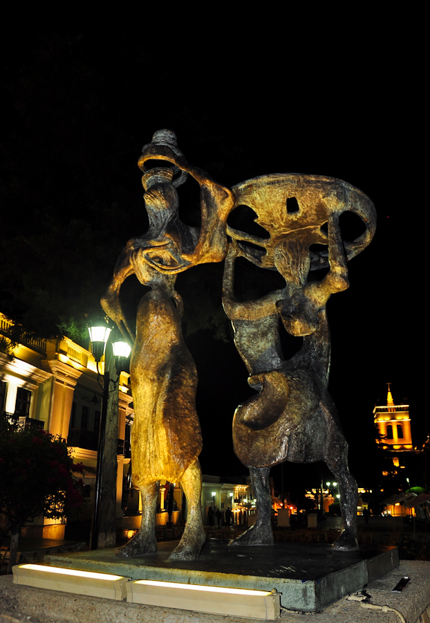 the statue shows two dancing women near a large building