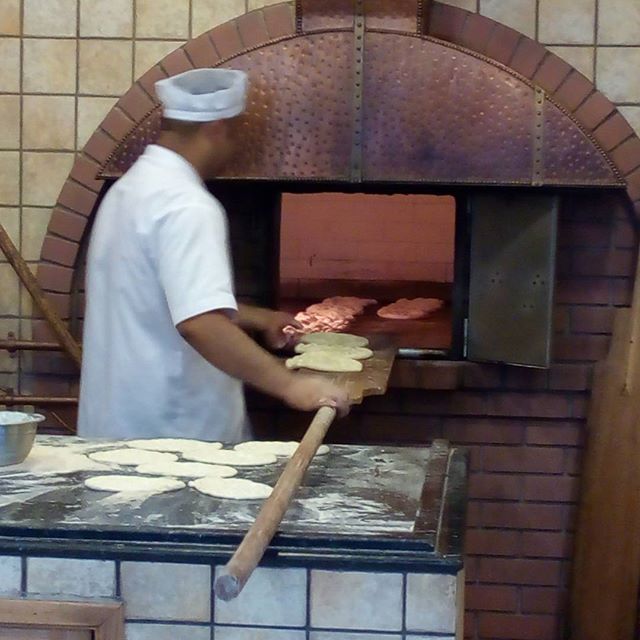 a cook prepares some meat inside of a wood fired oven
