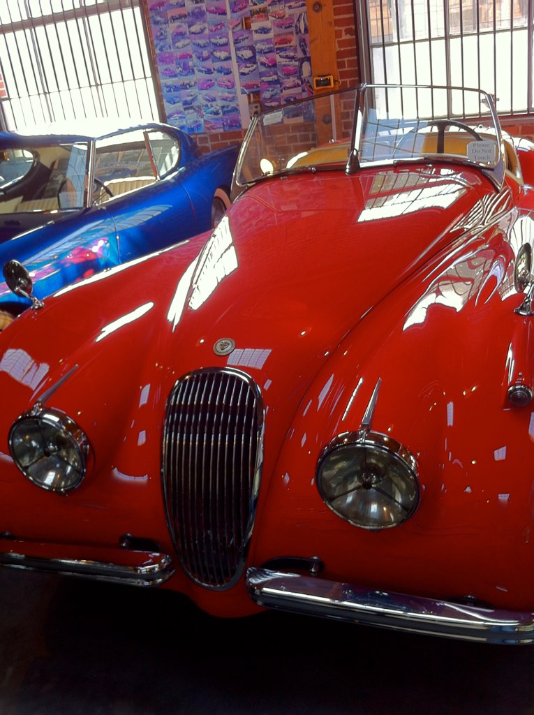 a red car in a showroom next to other old cars