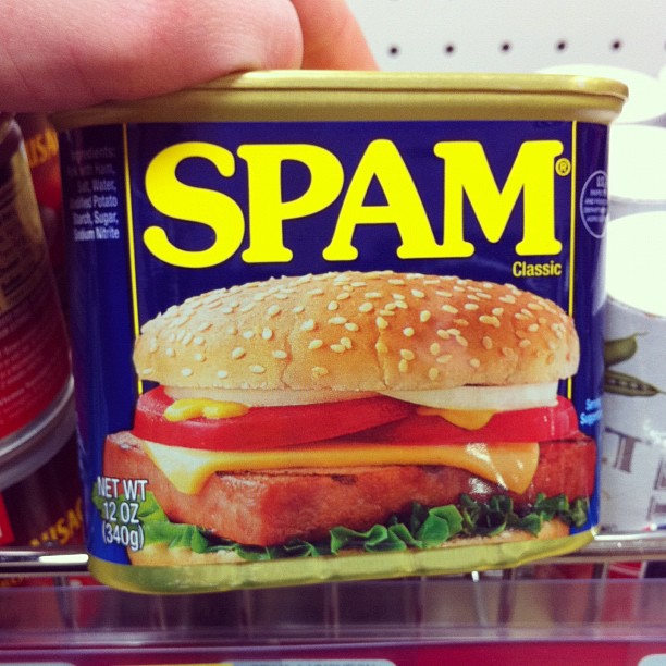 a hand is holding a can of spam with a chicken sandwich inside