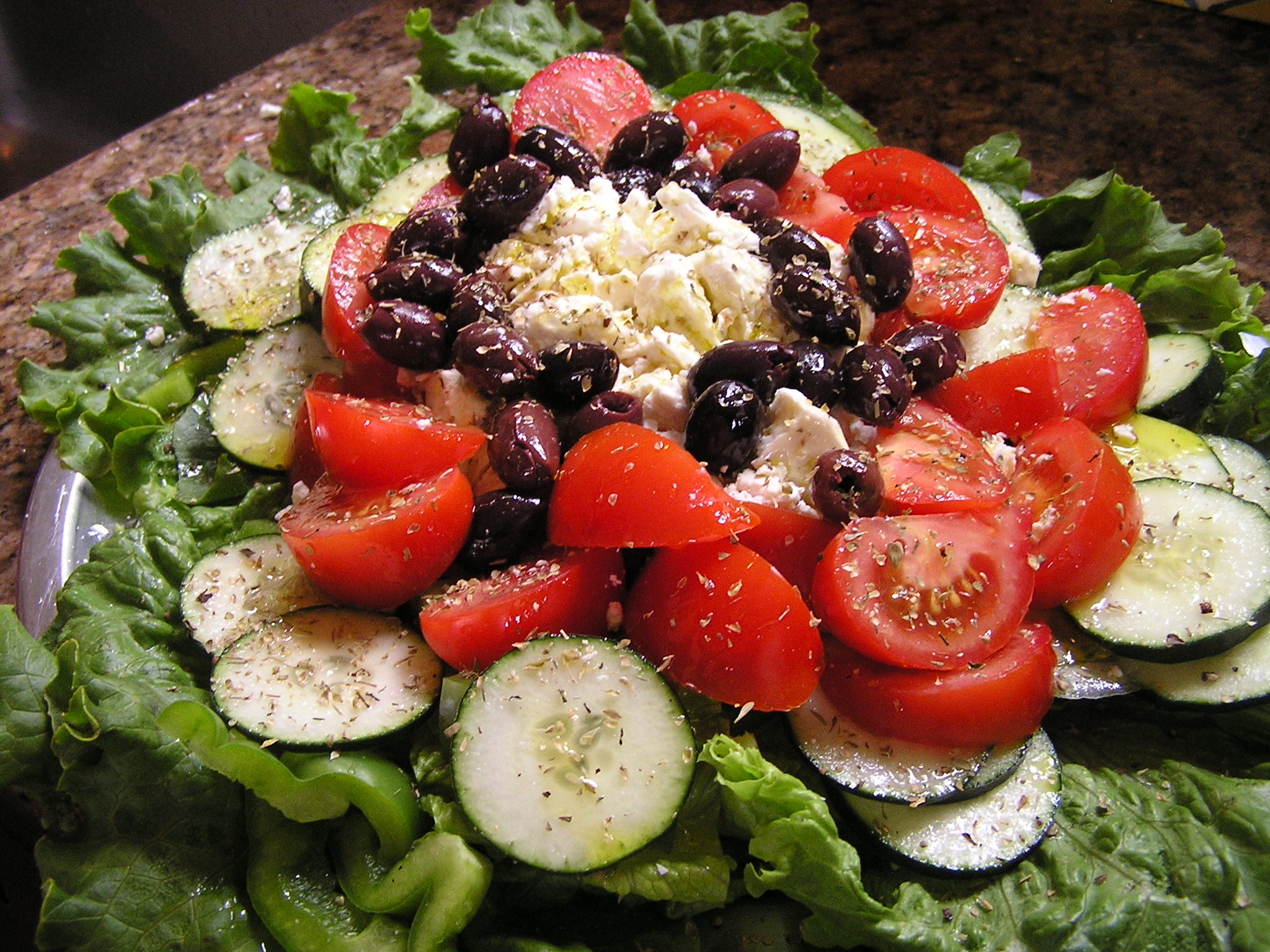 a bowl filled with lettuce, cucumber, tomato and other food items