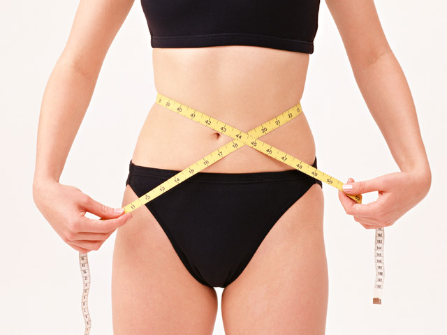 the female in a bikini holds a measuring tape over her waist