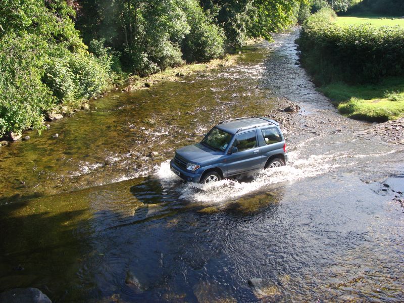 the car is driving through a stream, crossing