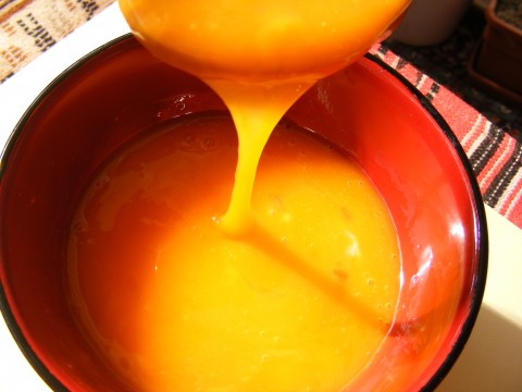 a ladle with an orange liquid pouring into a red bowl