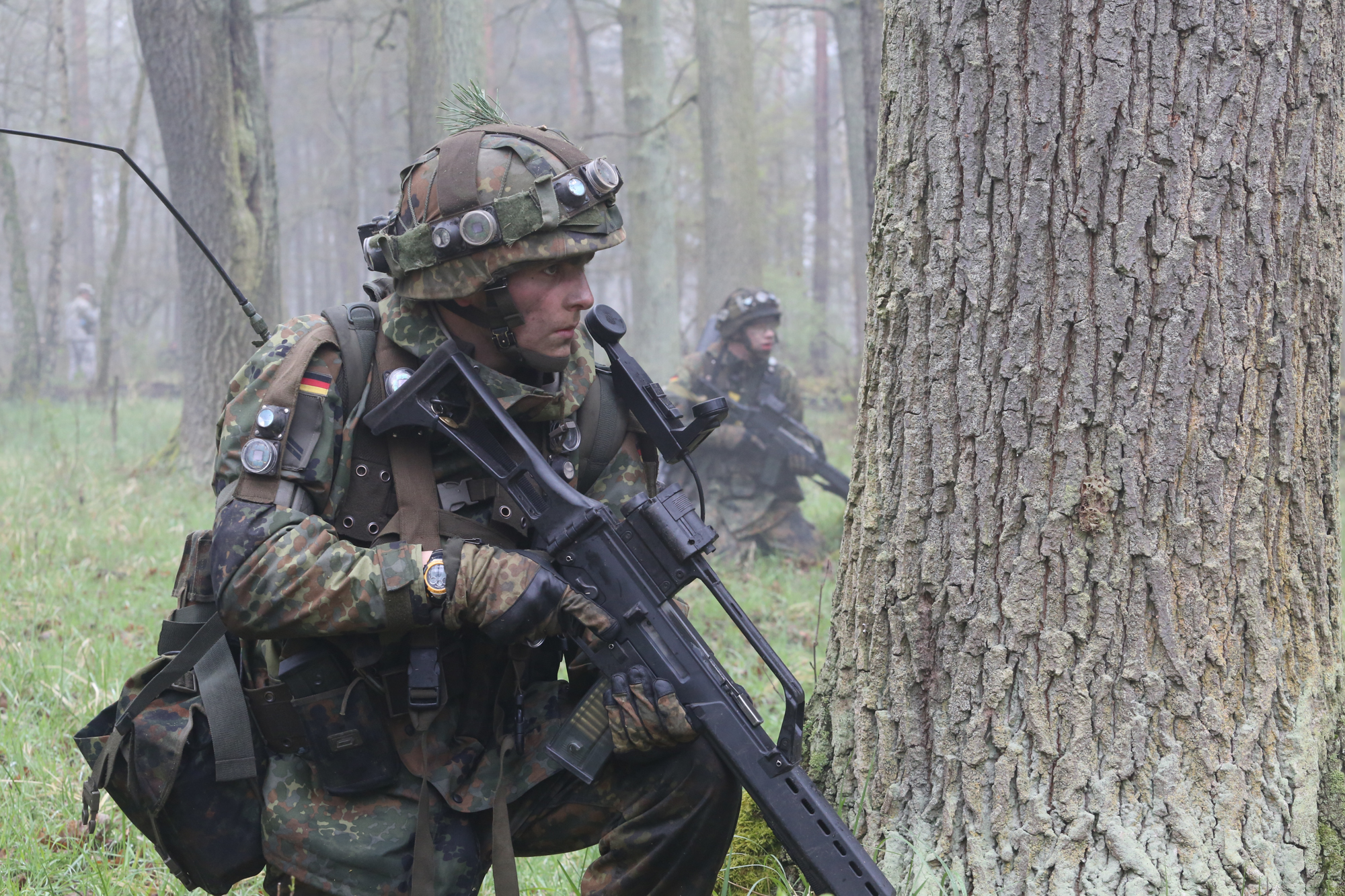 soldiers with weapons and backpacks taking cover under a tree