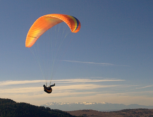 a man flying a yellow parachute over a lush green hillside