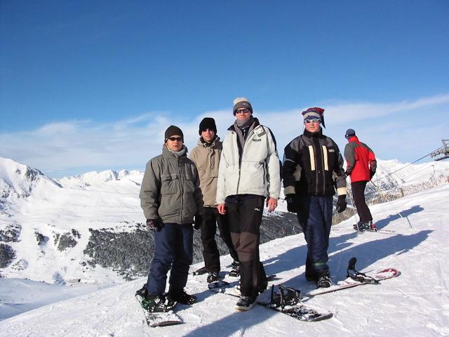 three men and one woman are standing on a snowy slope, with snow skis