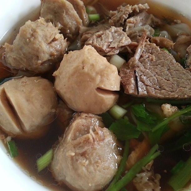 a soup in a white bowl with meat, vegetables and mushrooms