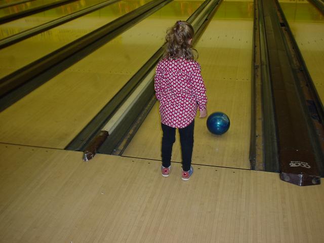 a girl in a pink and white jacket about to bowl a bowling ball