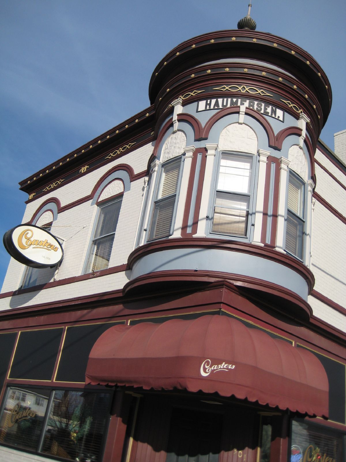 a large white building with red trim and a brown awning