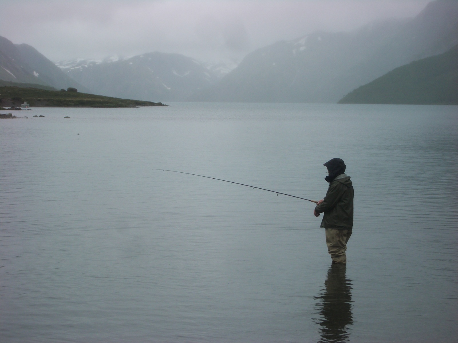 a man fishing on the lake in an overcast day