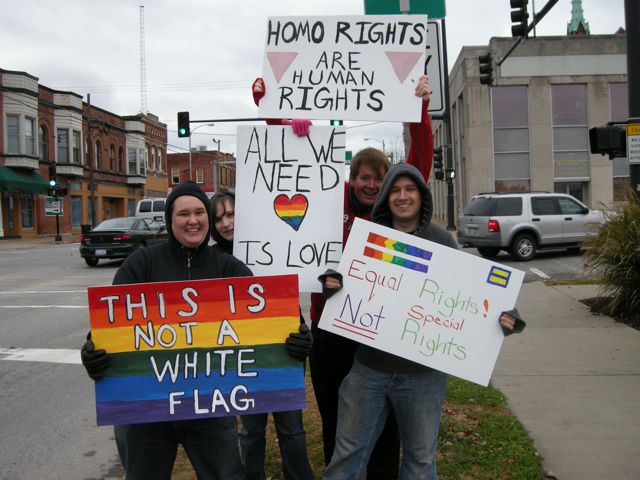 four people are standing outside holding signs