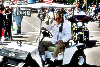 a man driving a golf cart down a street filled with people
