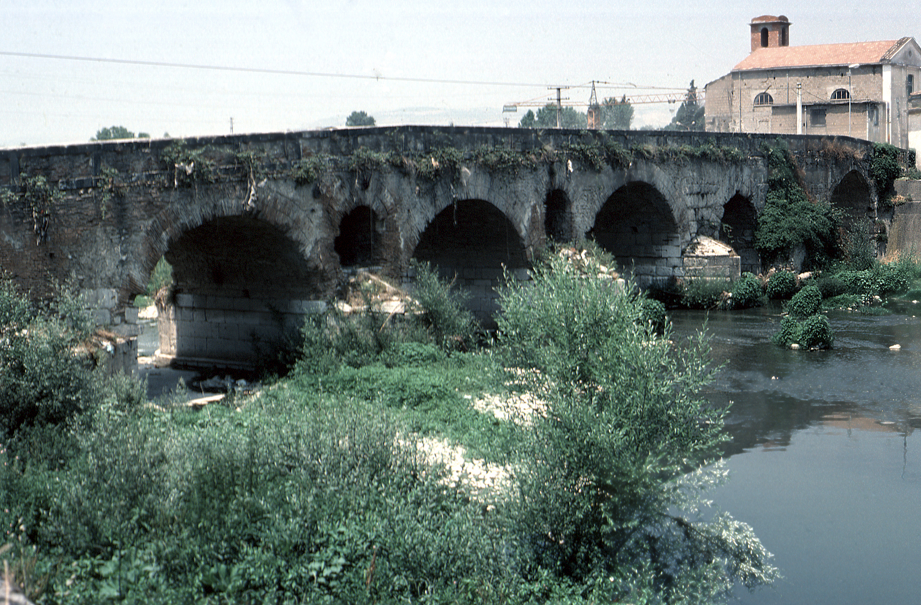 an old stone bridge with plants growing over the top