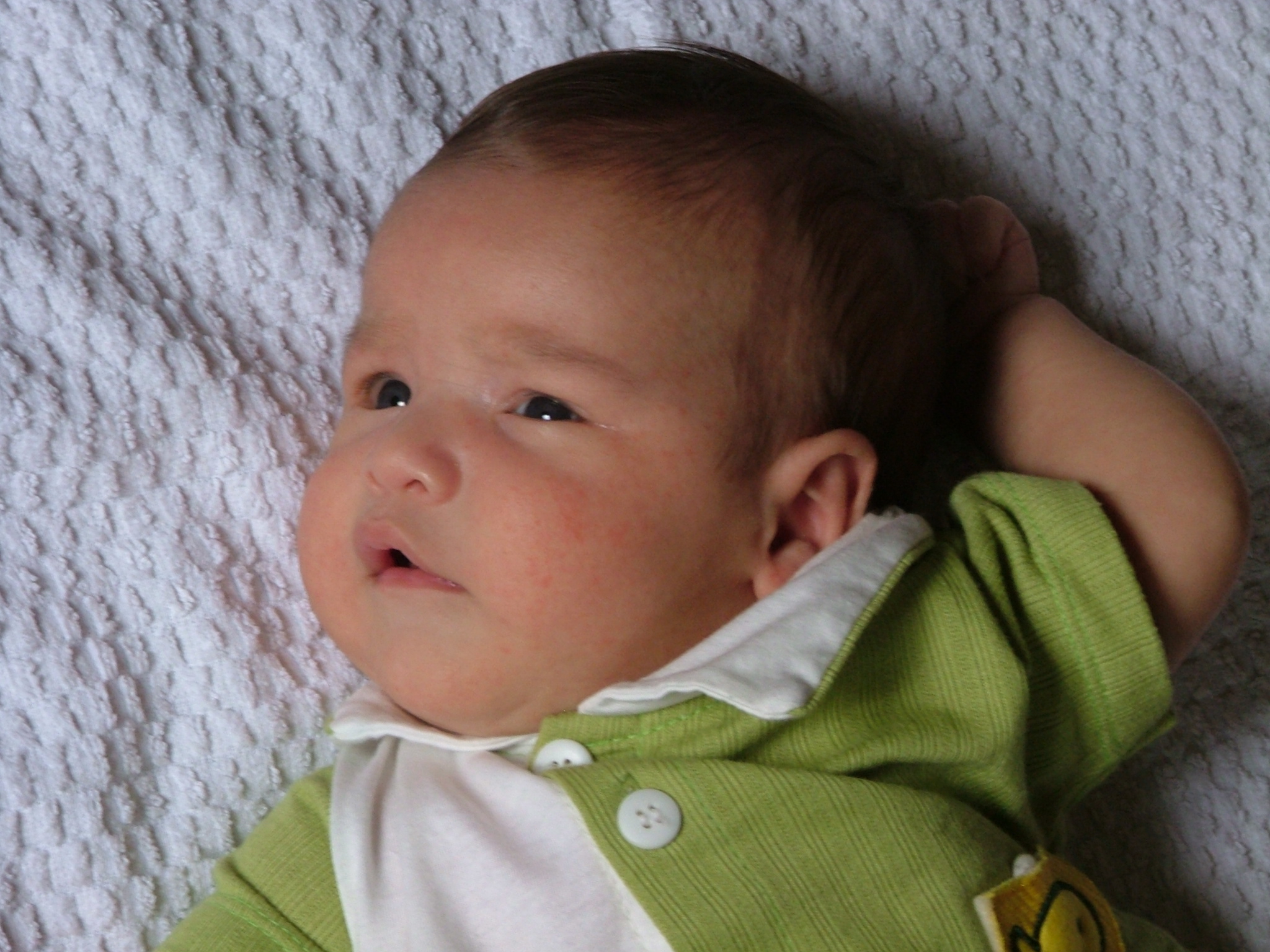 an adorable baby lays on his back with one arm under his head