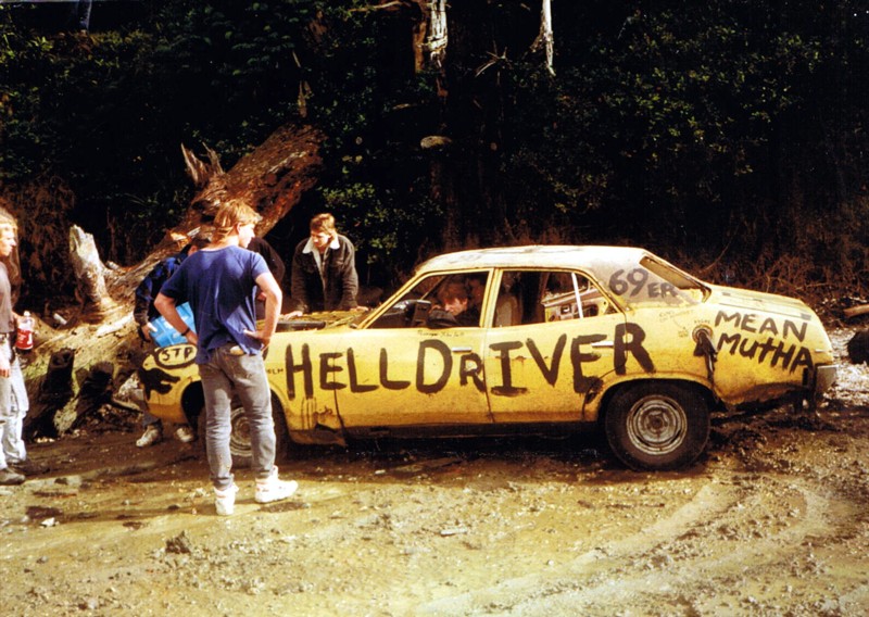 a group of young people standing around a wrecked car