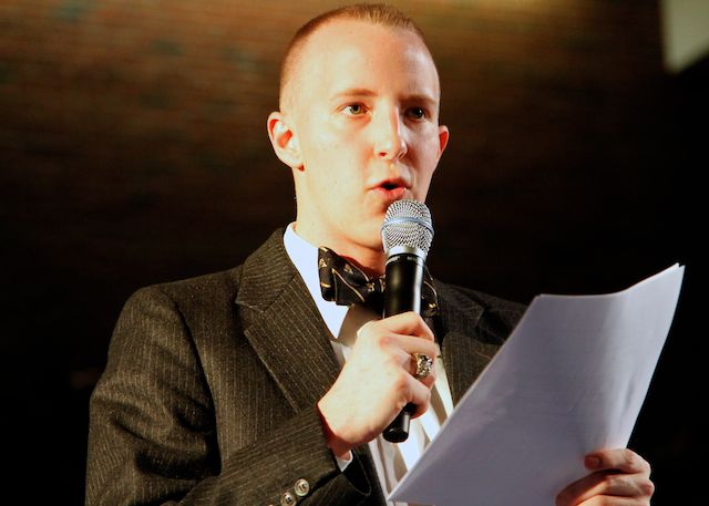 a young man dressed in a suit holding a microphone and paperwork