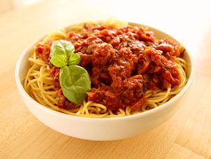 a bowl filled with spaghetti with sauce, meat and basil