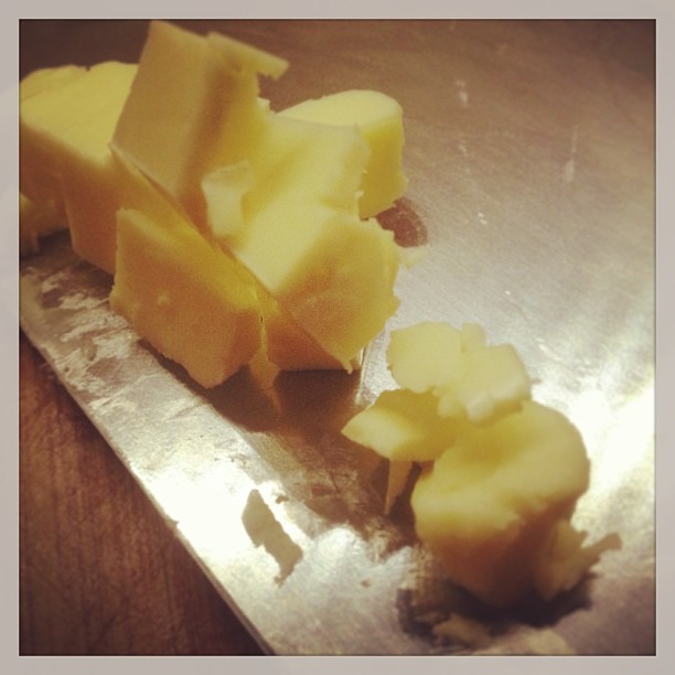 a knife sits on a metal  board with pieces of cheese