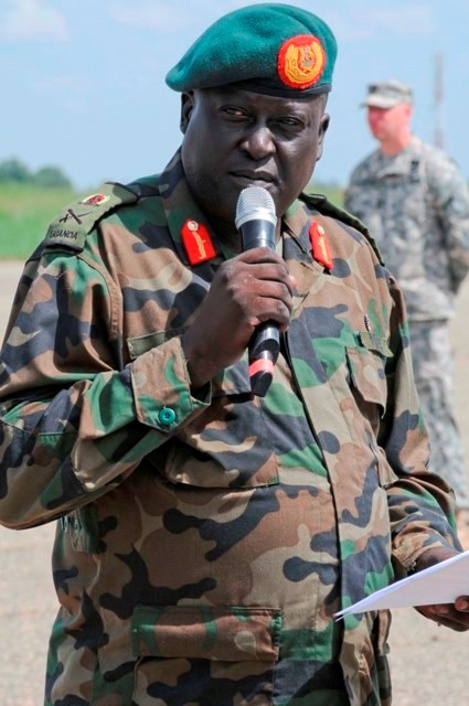 a soldier standing with microphone in hand and other people in background