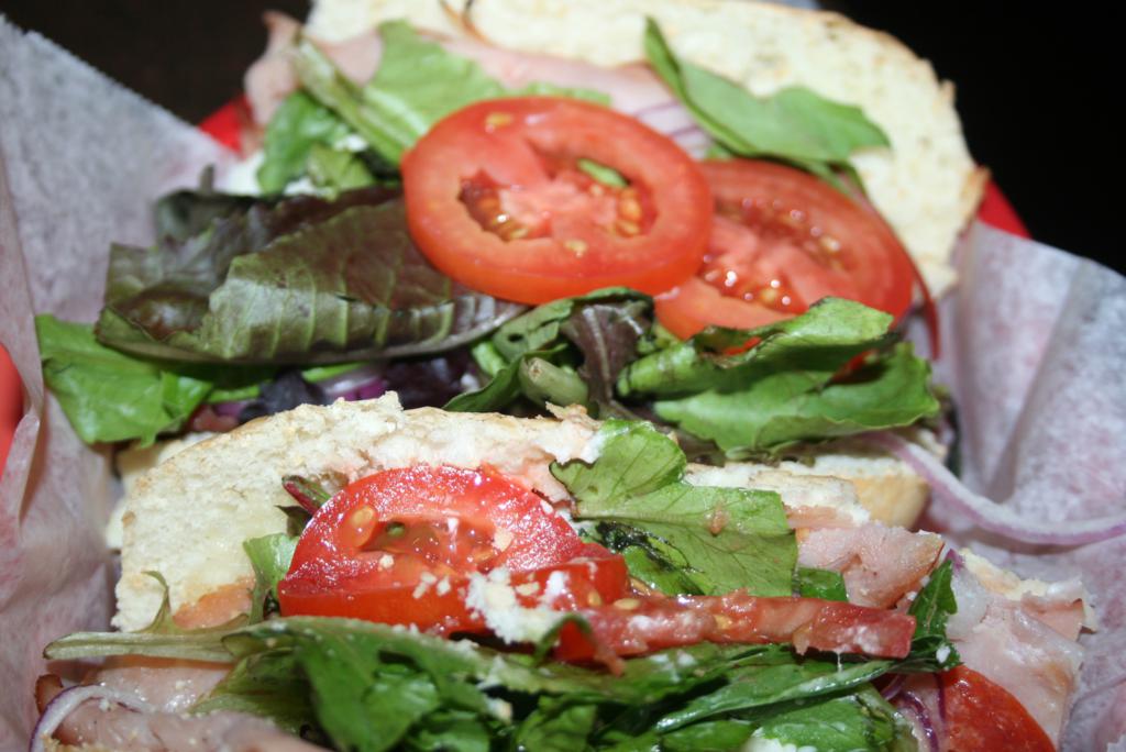 two sandwiches on a tray with tomatoes, lettuce and other foods