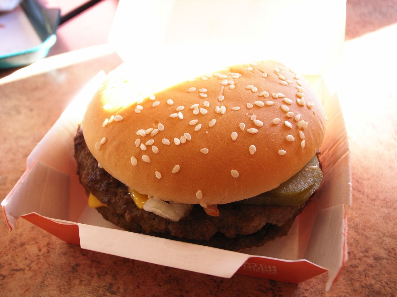 a cheeseburger in a paper container with toppings